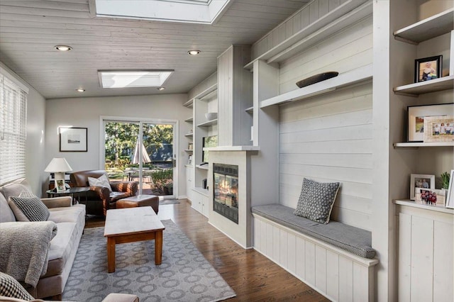 living area featuring a glass covered fireplace, recessed lighting, dark wood-type flooring, built in features, and a skylight