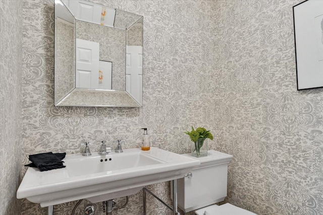 bathroom with toilet, wallpapered walls, and a sink