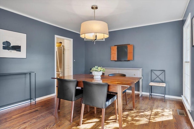 dining space featuring wood finished floors, visible vents, crown molding, and baseboards