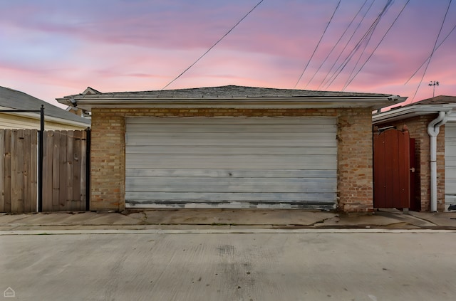 garage at dusk featuring fence