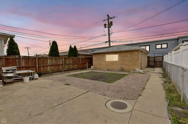 back of property at dusk featuring a patio, a fenced backyard, and brick siding