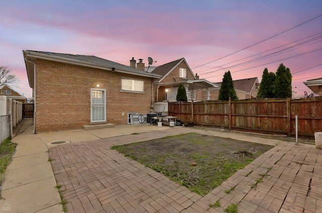 back of house at dusk with a chimney, a patio area, brick siding, and a fenced backyard