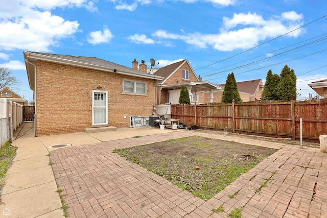 back of property with a chimney, a patio area, brick siding, and a fenced backyard
