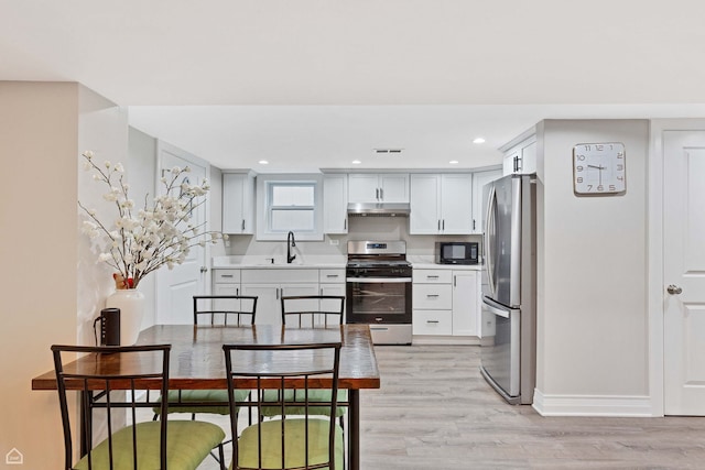 kitchen with stainless steel appliances, under cabinet range hood, light countertops, baseboards, and light wood-type flooring