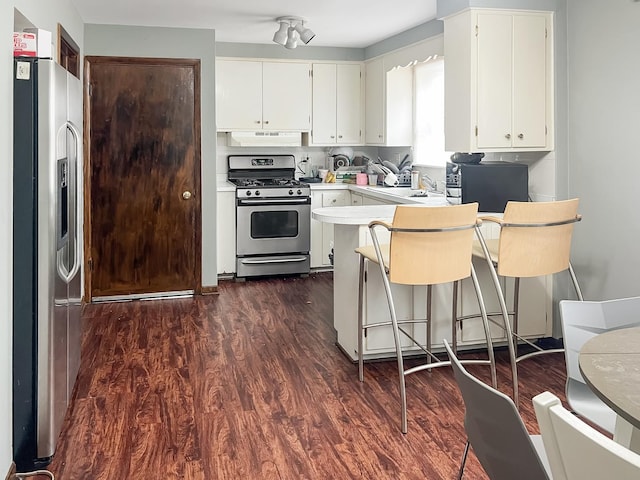 kitchen with a peninsula, appliances with stainless steel finishes, under cabinet range hood, and dark wood-type flooring