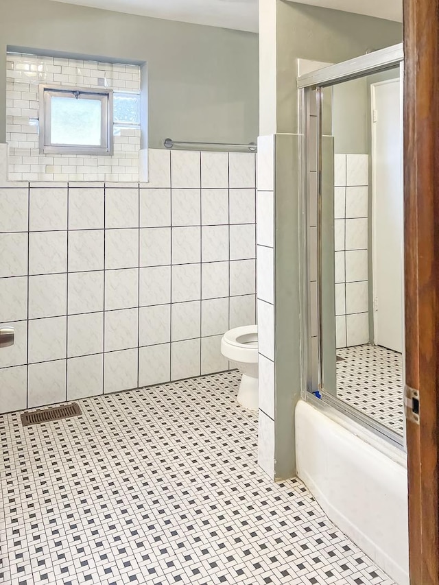 full bathroom featuring tile patterned floors, a shower with door, tile walls, toilet, and visible vents