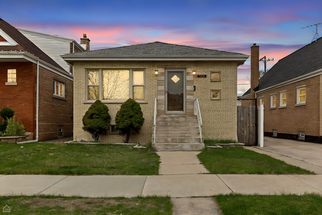 bungalow-style house featuring brick siding, entry steps, and a front lawn