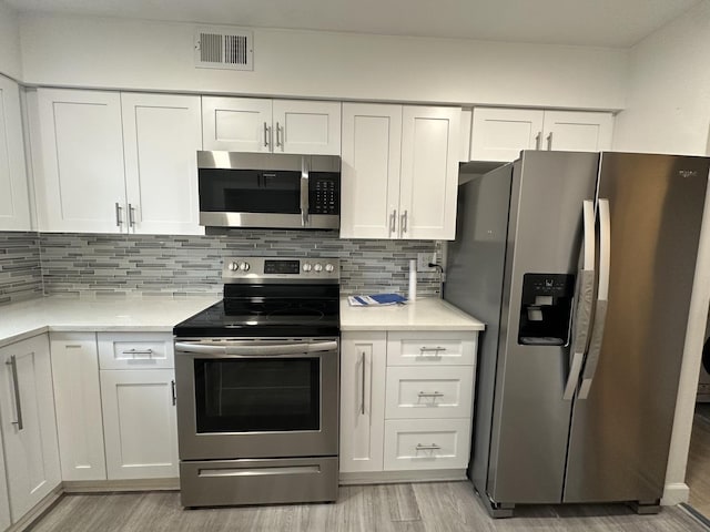 kitchen with tasteful backsplash, visible vents, white cabinets, appliances with stainless steel finishes, and light wood-style floors