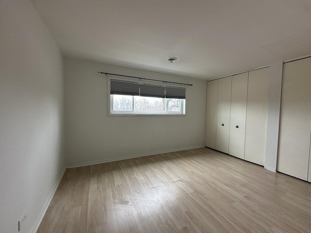 unfurnished bedroom with multiple closets, light wood-style flooring, baseboards, and visible vents
