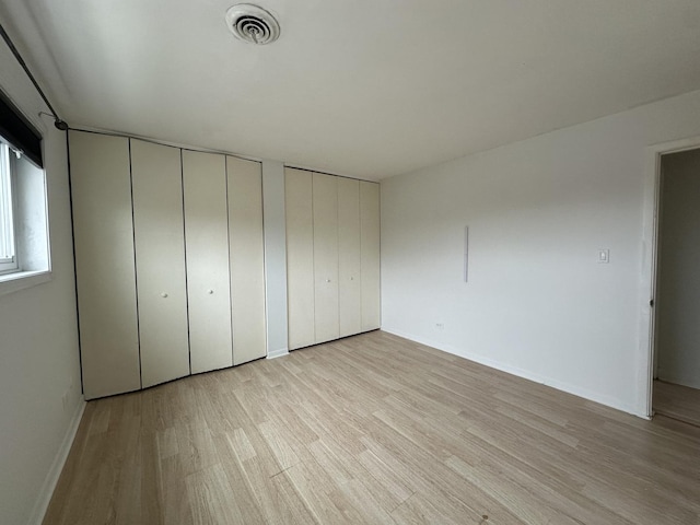 unfurnished bedroom featuring light wood finished floors, visible vents, baseboards, and multiple closets