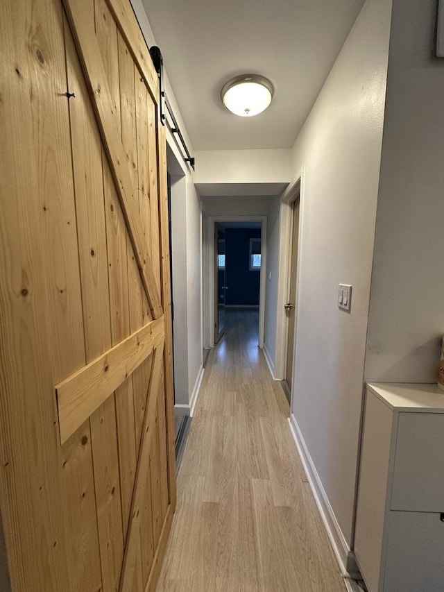 hallway featuring baseboards, light wood finished floors, and a barn door