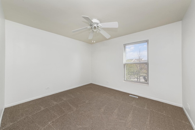 empty room featuring baseboards, dark carpet, and a ceiling fan