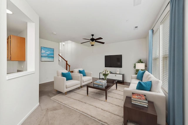 carpeted living room with ceiling fan, baseboards, visible vents, and stairs