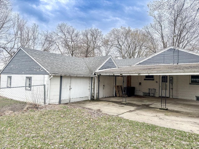 rear view of property featuring a carport, roof with shingles, driveway, and fence