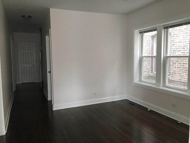unfurnished room featuring baseboards, dark wood-style flooring, and visible vents
