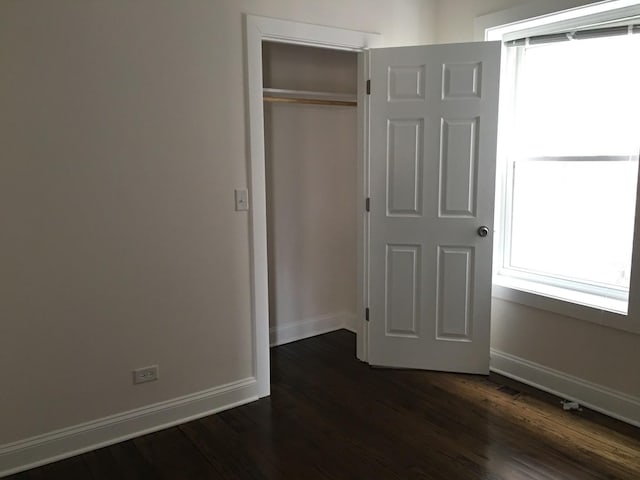 unfurnished bedroom with baseboards, a closet, and dark wood-style flooring