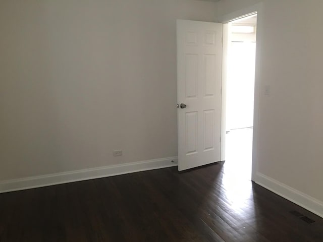 unfurnished room featuring baseboards, dark wood-style floors, and visible vents
