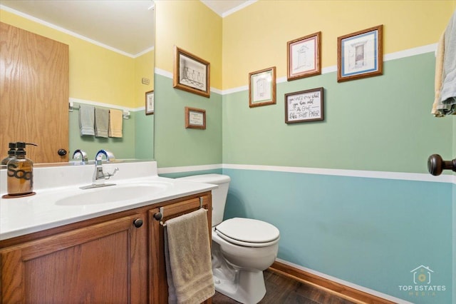 half bathroom featuring vanity, baseboards, ornamental molding, toilet, and wood finished floors