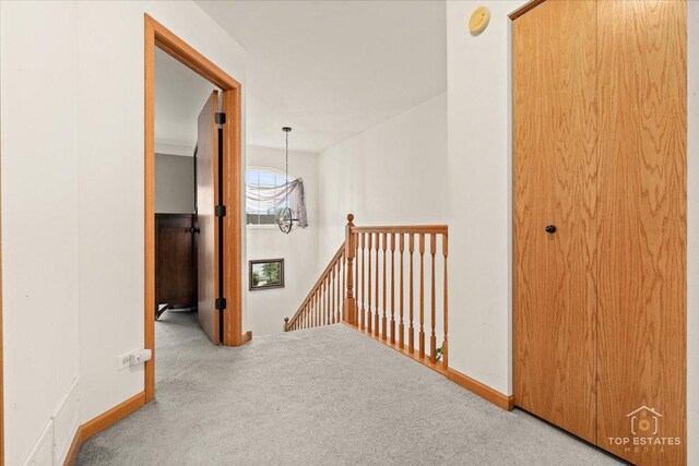 hall featuring carpet flooring, baseboards, and an upstairs landing