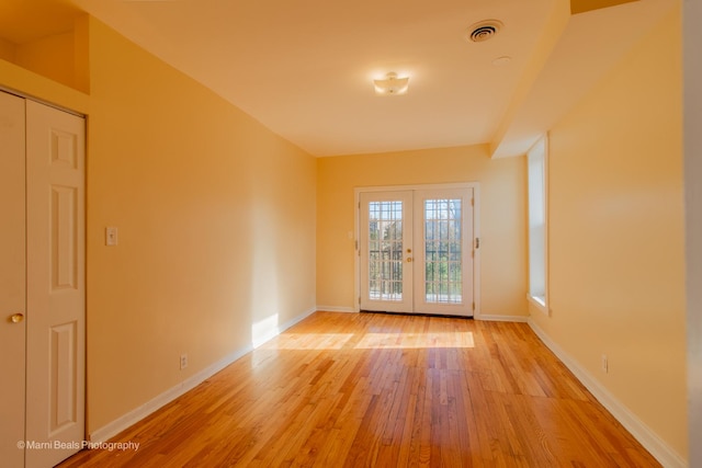 empty room with light wood-style flooring, french doors, baseboards, and visible vents