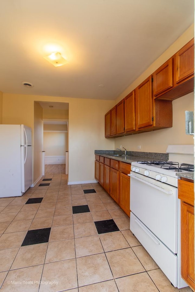 kitchen featuring light tile patterned floors, white appliances, a sink, brown cabinets, and baseboards