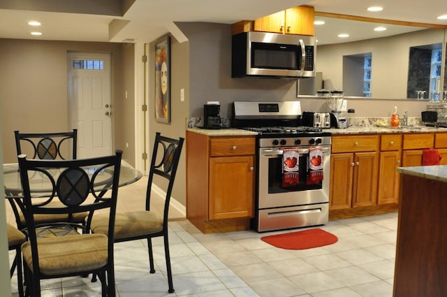 kitchen with light tile patterned floors, recessed lighting, light stone counters, stainless steel appliances, and brown cabinets