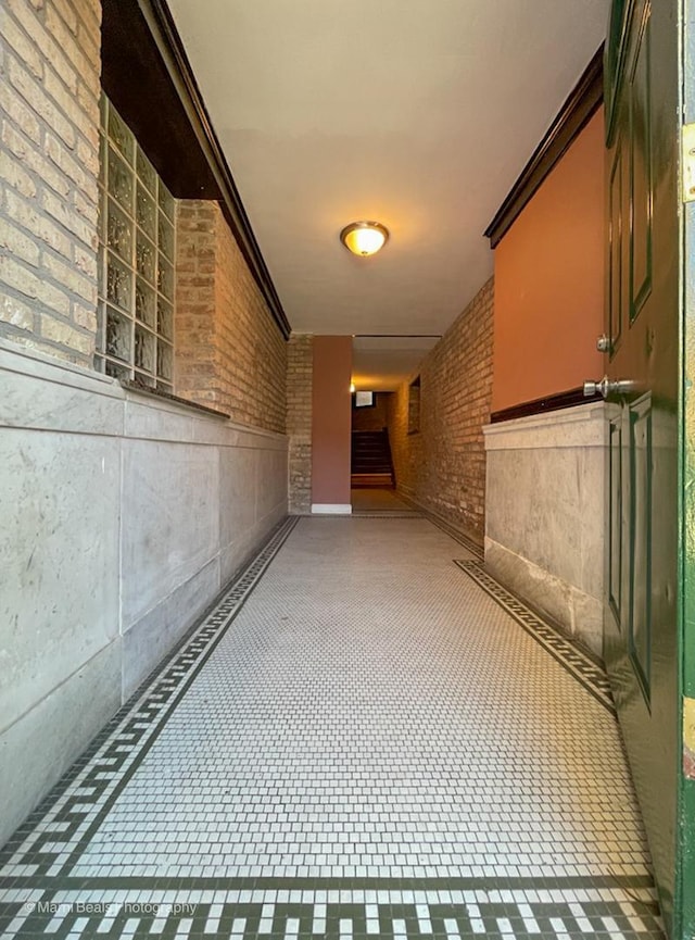 hall featuring crown molding, brick wall, and stairway