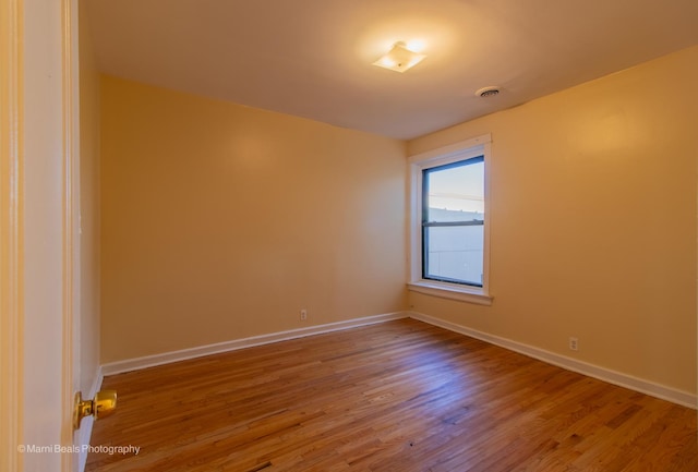 empty room with wood finished floors, baseboards, and visible vents