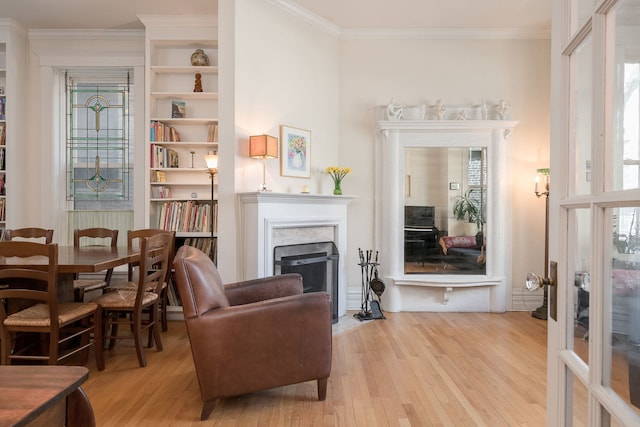 living area featuring a fireplace with flush hearth, light wood-style flooring, and crown molding