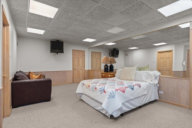 carpeted bedroom with wood walls, a wainscoted wall, and a paneled ceiling