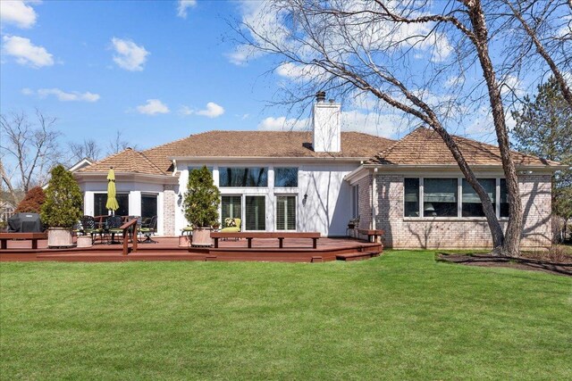 rear view of house featuring a chimney, a wooden deck, brick siding, and a yard