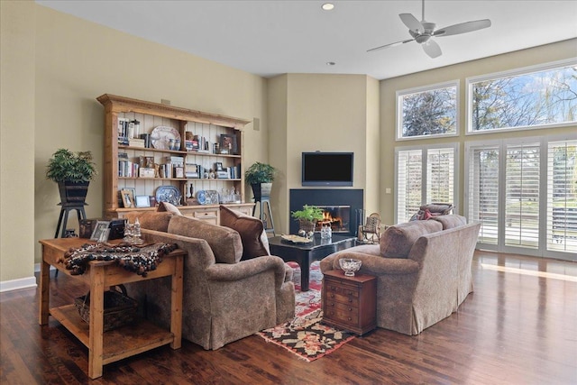 living room featuring a ceiling fan, a glass covered fireplace, baseboards, dark wood-type flooring, and recessed lighting