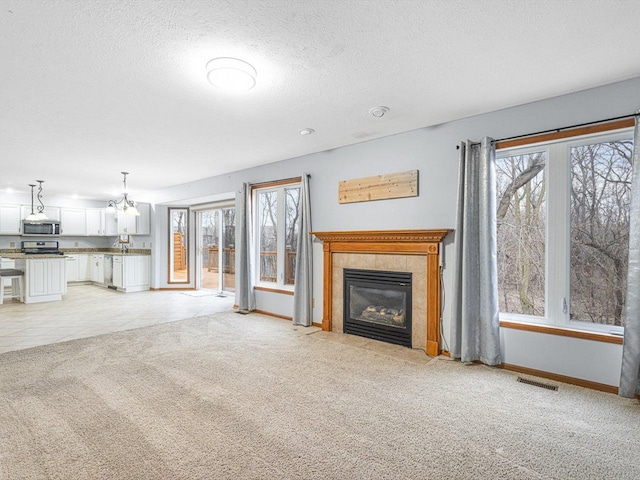 2072 Charnwood Ct, Machesney Park, IL 61115 - unfurnished living room with a textured ceiling, light colored carpet, visible vents, a tile fireplace, and baseboards