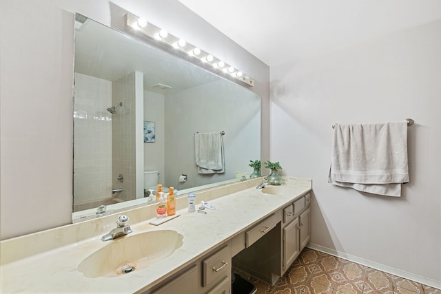full bathroom with toilet, double vanity, a sink, and baseboards