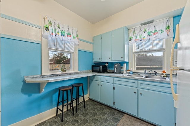 kitchen with freestanding refrigerator, black microwave, blue cabinetry, light countertops, and a sink