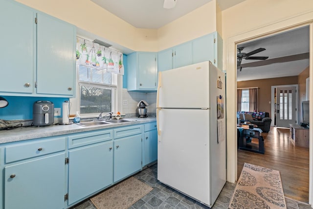kitchen with a sink, freestanding refrigerator, blue cabinetry, and a ceiling fan