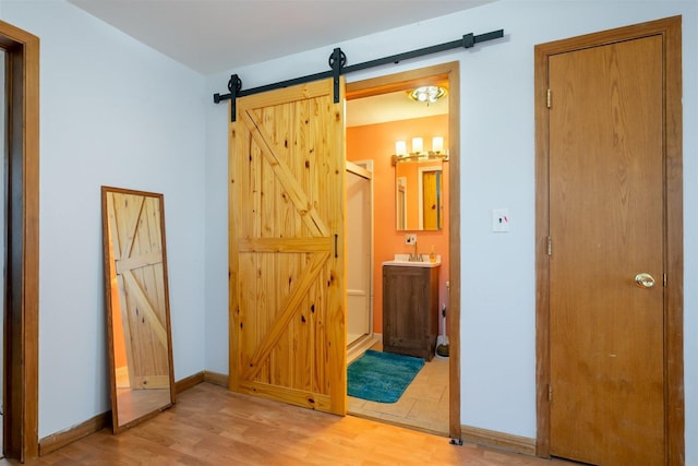 hall with a barn door, light wood-type flooring, and baseboards