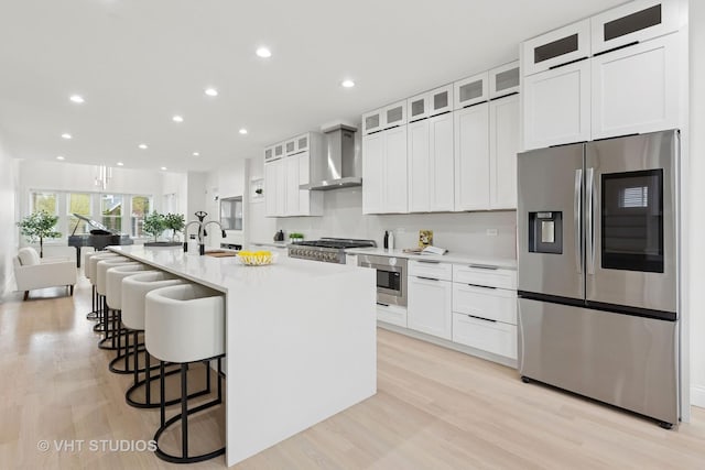 7440 S Oglesby Ave, Chicago, IL 60649 - kitchen featuring appliances with stainless steel finishes, wall chimney exhaust hood, light wood-style flooring, a kitchen bar, and white cabinetry