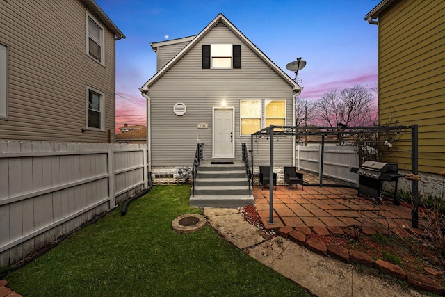 back of house at dusk with a patio area, a yard, and fence