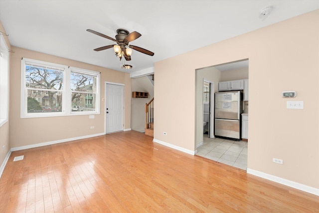 empty room with light wood-style floors, baseboards, a ceiling fan, and stairway