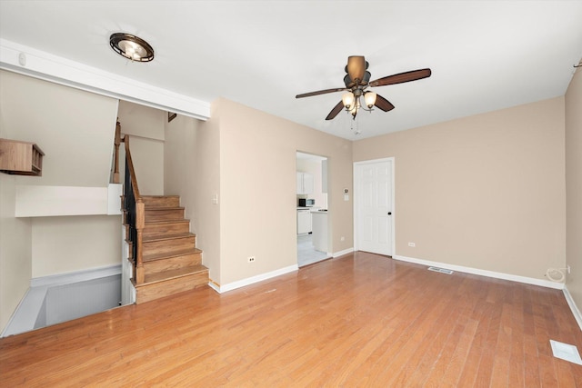 unfurnished living room featuring visible vents, baseboards, ceiling fan, stairway, and wood finished floors