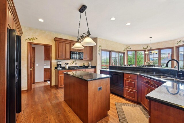 kitchen with black appliances, a kitchen island, a sink, light wood-style floors, and a chandelier