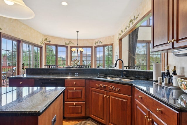 kitchen featuring a sink, a chandelier, decorative light fixtures, a peninsula, and dark stone counters