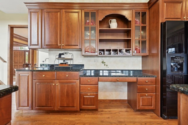 kitchen with black fridge with ice dispenser, light wood-style floors, brown cabinets, glass insert cabinets, and dark stone counters