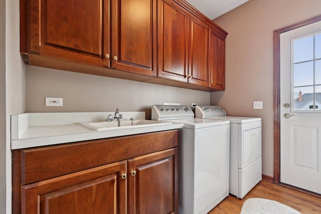 clothes washing area with washing machine and clothes dryer, cabinet space, and light wood finished floors