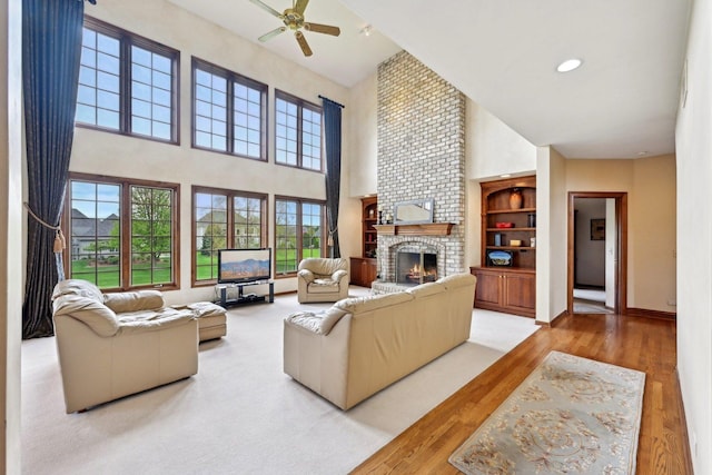 living area with a towering ceiling, a fireplace, a ceiling fan, wood finished floors, and baseboards