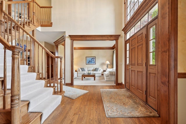 foyer featuring a high ceiling, baseboards, stairway, wood finished floors, and crown molding
