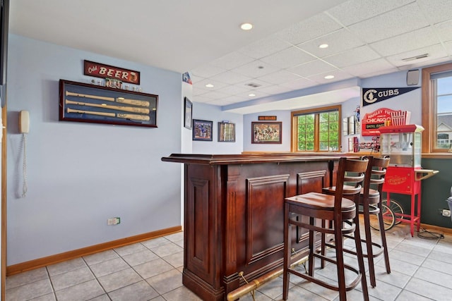 indoor dry bar featuring a drop ceiling, baseboards, healthy amount of natural light, and light tile patterned floors
