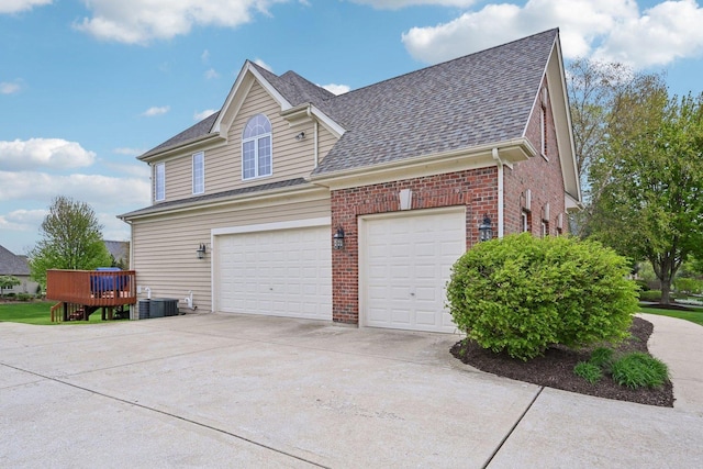 view of side of property featuring brick siding, driveway, a shingled roof, central air condition unit, and a wooden deck