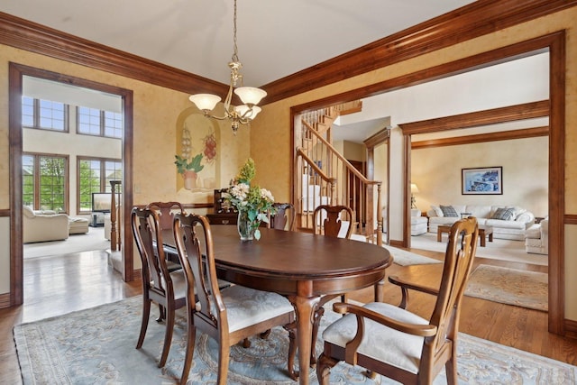 dining area featuring wood finished floors, stairs, crown molding, a chandelier, and baseboards